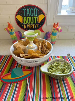 Taco-themed party setup with chips, guacamole, and decorative signs on a striped tablecloth.