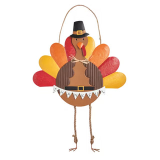 A decorative hanging turkey ornament with a brown body, multicolored feather shapes in red, orange, and yellow, a black pilgrim hat, rope legs, and a small 'Thankful' banner.