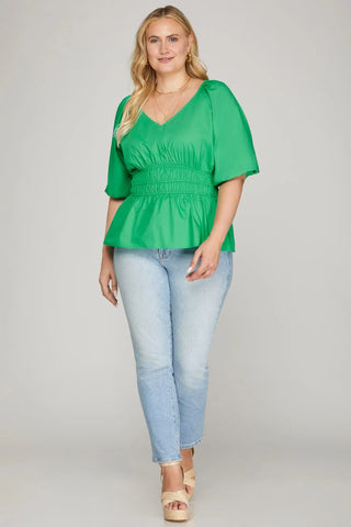 Woman wearing a green blouse and light blue jeans on a gray background