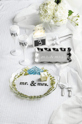 Wedding table setting with 'Mr.' and 'Mrs.' signs, candles, and flowers on a white tablecloth.