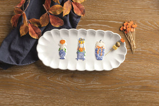 Decorative white platter with painted vases on a wooden surface with fall leaves and carrots.