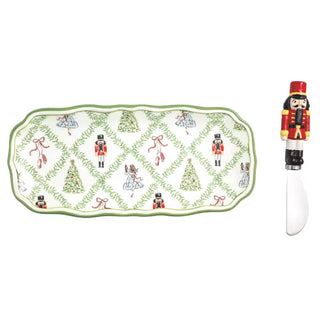 A holiday-themed ceramic serving tray with a matching nutcracker-shaped knife, featuring a white background decorated with green ivy, Christmas trees, and nutcracker figures.