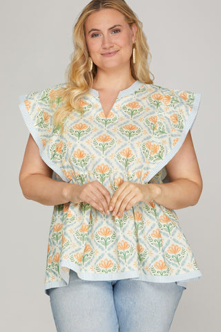 Woman wearing a floral patterned top with ruffled shoulders on a plain background