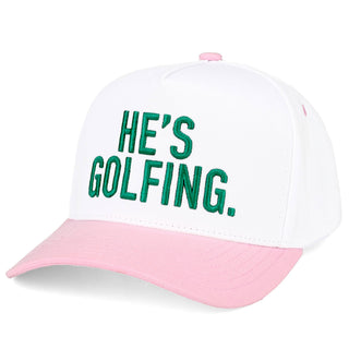 White and pink cap with green text 'HE'S GOLFING.' on a white background