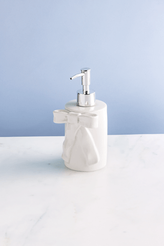 White ceramic soap dispenser with silver pump on a white surface and light blue background