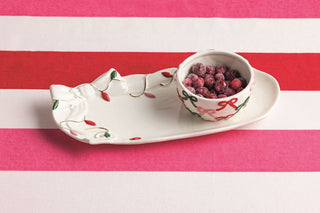 White ceramic leaf-shaped dish with a small bowl of raspberries on a pink and white striped background