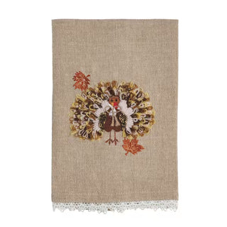 A beige linen tea towel with a white lace trim at the bottom, featuring a central embroidered turkey design surrounded by autumn leaves.