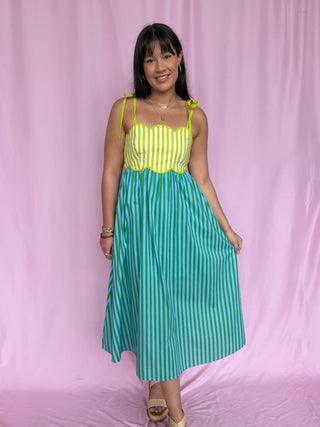 Woman wearing a yellow and green striped dress against a pink background