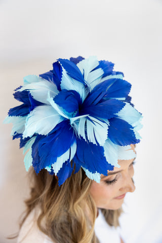 Woman wearing a blue and white feathered headpiece against a plain background