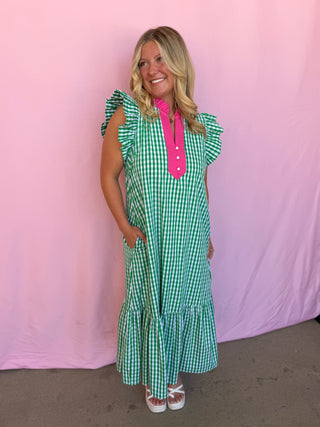 Woman wearing a green and white checkered dress with a pink shirt underneath against a pink background