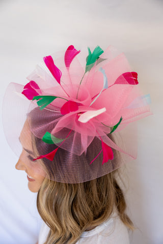 Woman wearing a decorative pink and green headpiece against a white background