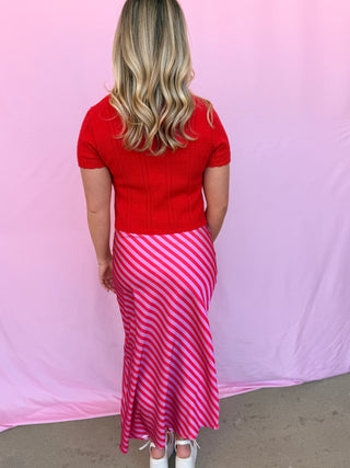 Person wearing a red top and pink striped skirt against a pink background
