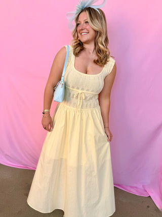 Woman in a light yellow dress with a blue handbag against a pink and purple gradient background