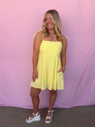 Woman wearing a yellow polka dot dress against a pink background