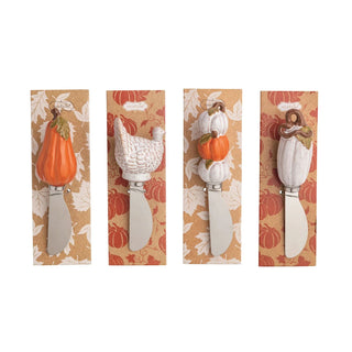 Four decorative cheese knives with autumn-themed handles are displayed on their original patterned backing cards against a white background.