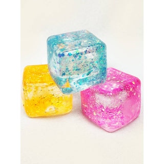 Three colorful glittery ice cubes on a white background