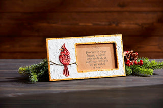 Decorative plaque with cardinal design and text on a wooden surface with greenery.
