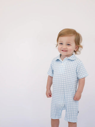Child wearing a light blue checkered romper on a white background