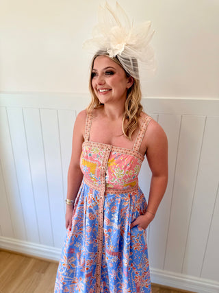 Woman wearing a colorful floral dress with a large decorative headpiece against a white paneled wall.
