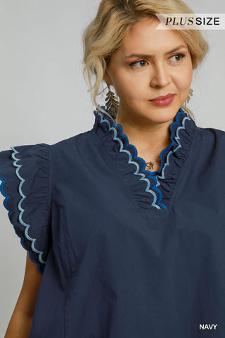 Woman wearing a navy blouse with blue ruffled details on a gray background