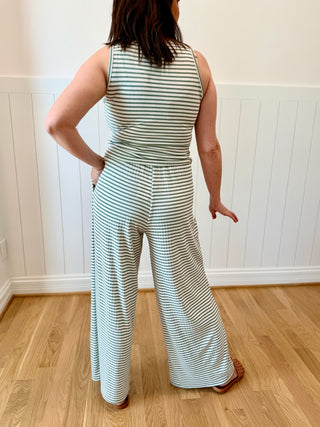Person wearing a striped jumpsuit standing in a room with wooden flooring and white walls.