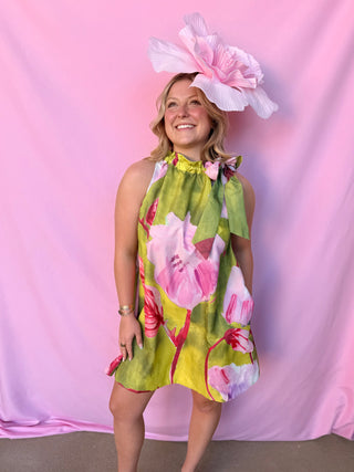 Woman wearing a floral dress and large hat against a pink background