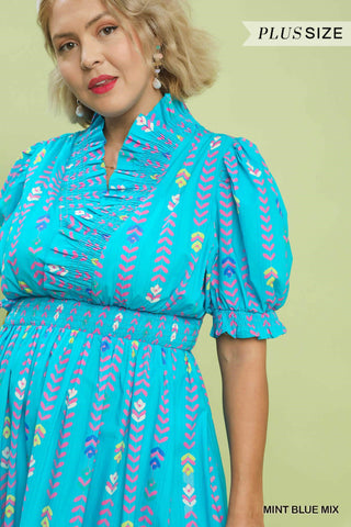 Woman wearing a turquoise dress with colorful patterns on a light green background