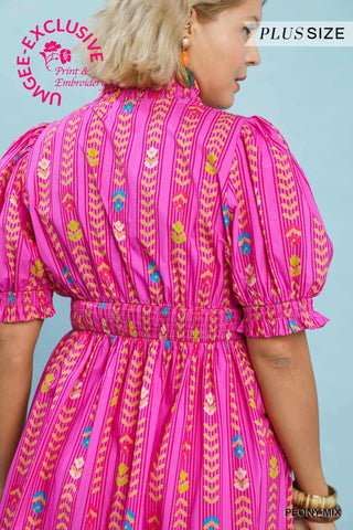 Woman wearing a pink dress with colorful patterns on a light blue background