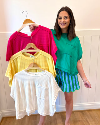 Woman holding a pink shirt with three other shirts on hangers, standing against a white wall.