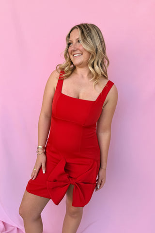Woman wearing a red dress with a large bow and a matching headpiece against a pink background