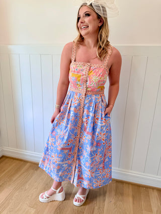 Woman wearing a colorful floral dress standing in a room with wooden flooring and white walls.