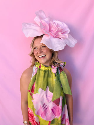Woman wearing a large pink floral hat against a pink background