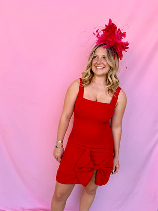 Woman wearing a red dress and matching fascinator against a pink background