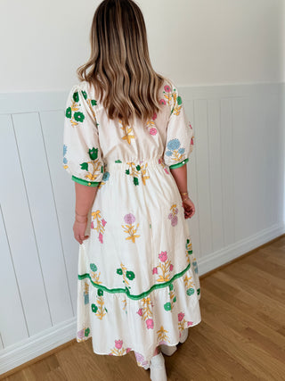 Woman wearing a floral dress standing in a room with wooden flooring and white walls.