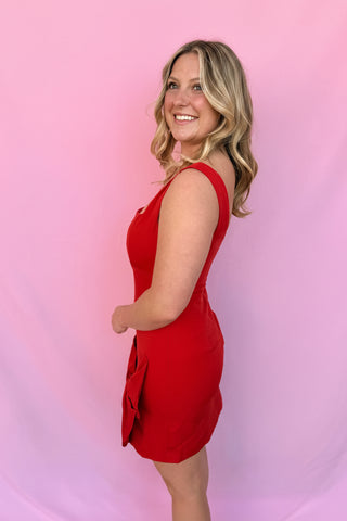 Woman wearing a red dress and matching fascinator against a pink background