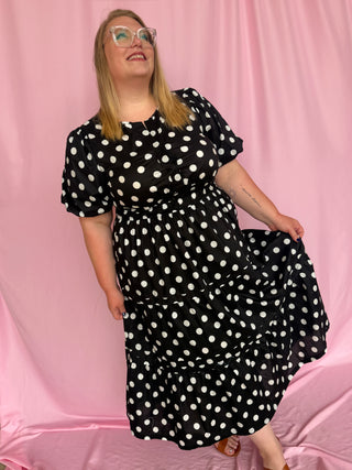 Woman wearing a black polka dot dress against a pink background