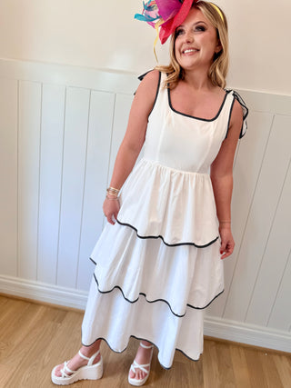 Woman wearing a white dress with black trim and a colorful hat indoors.