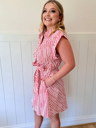 Woman wearing a red and white striped dress against a white paneled wall.