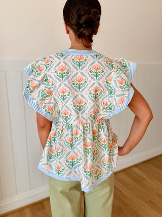 Person wearing a floral patterned apron with ruffled sleeves against a white wall.