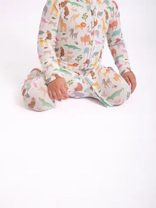 A child wearing a long-sleeve footed one-piece pajama with a colorful safari animal print, sitting cross-legged against a plain white background.