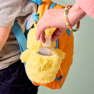Person holding a yellow plush toy with a small bottle attached, against a neutral background