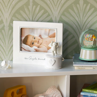 Decorative shelf with a photo frame, baby figurine, and books against a patterned wall.