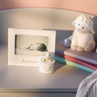 Decorative shelf with photo frame, small figurine, and toy sheep on a soft pink background