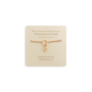Gold bracelet with a cross charm on a beige card with text, displayed against a white background.