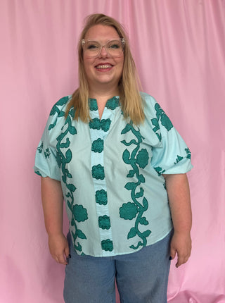 Person wearing a light blue blouse with green floral patterns on a pink background