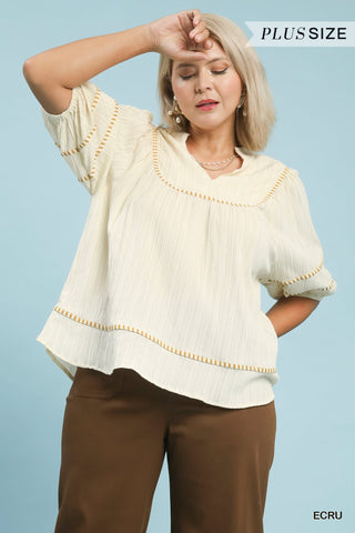 Woman wearing a beige blouse with decorative trim against a light blue background