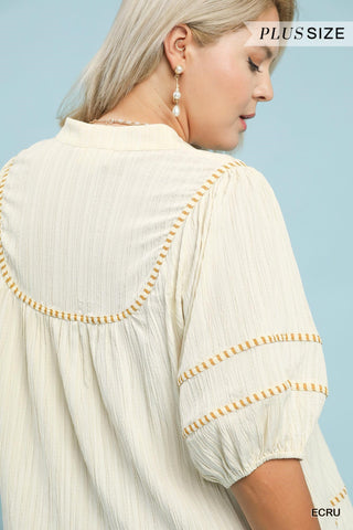 Woman wearing a beige blouse with decorative trim against a light blue background