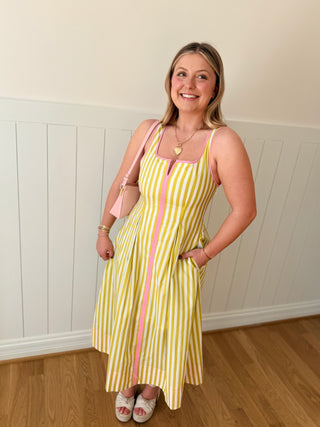 Woman wearing a lime and pink striped dress standing in a room with wooden flooring and white walls.