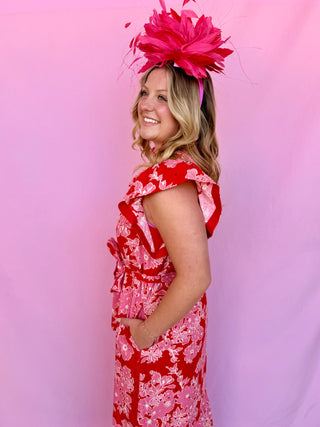 Woman wearing a red and pink floral dress with a large pink feathered headpiece against a pink background