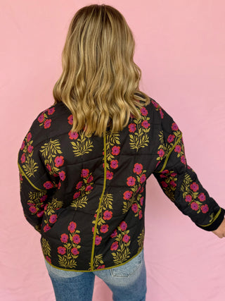 Person wearing a black floral embroidered jacket on a pink background